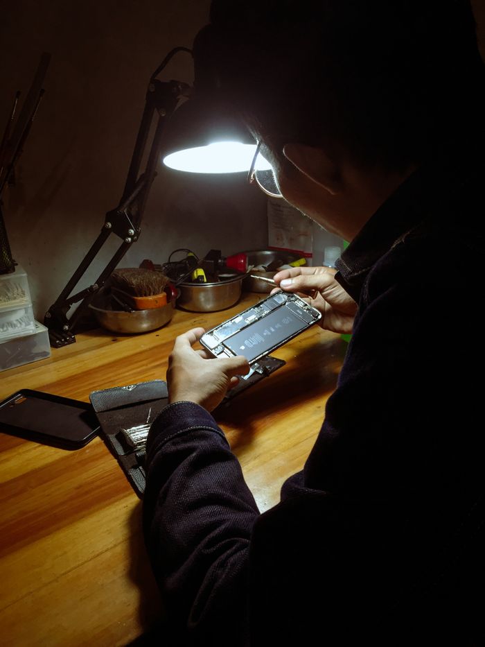 Crafting Captivating Headlines: Your awesome post title goes here An adult man repairing a smartphone under a desk lamp in a dimly lit room.